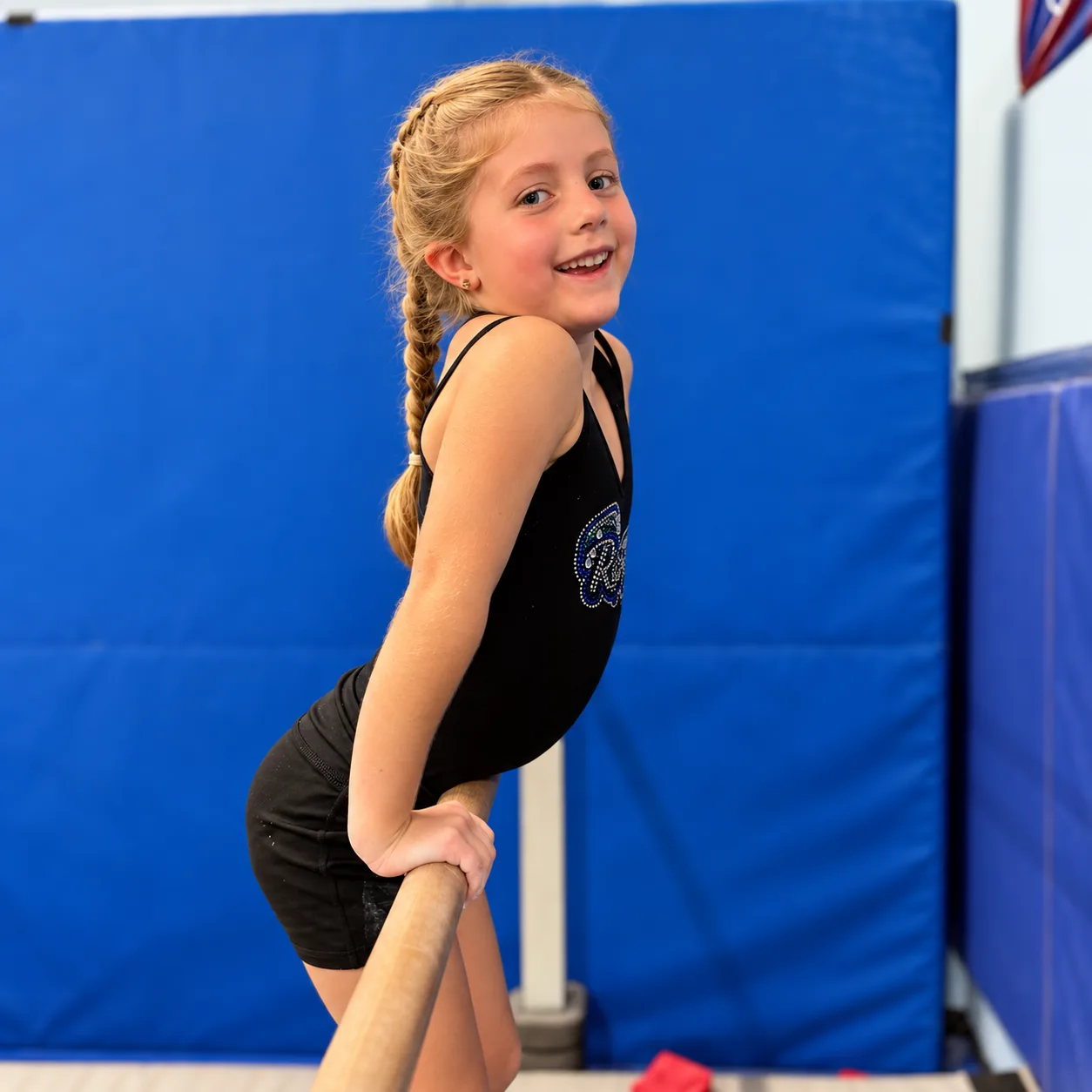 A smiling young gymnast supporting herself on a gymnastics bar at All 4 Prosper.